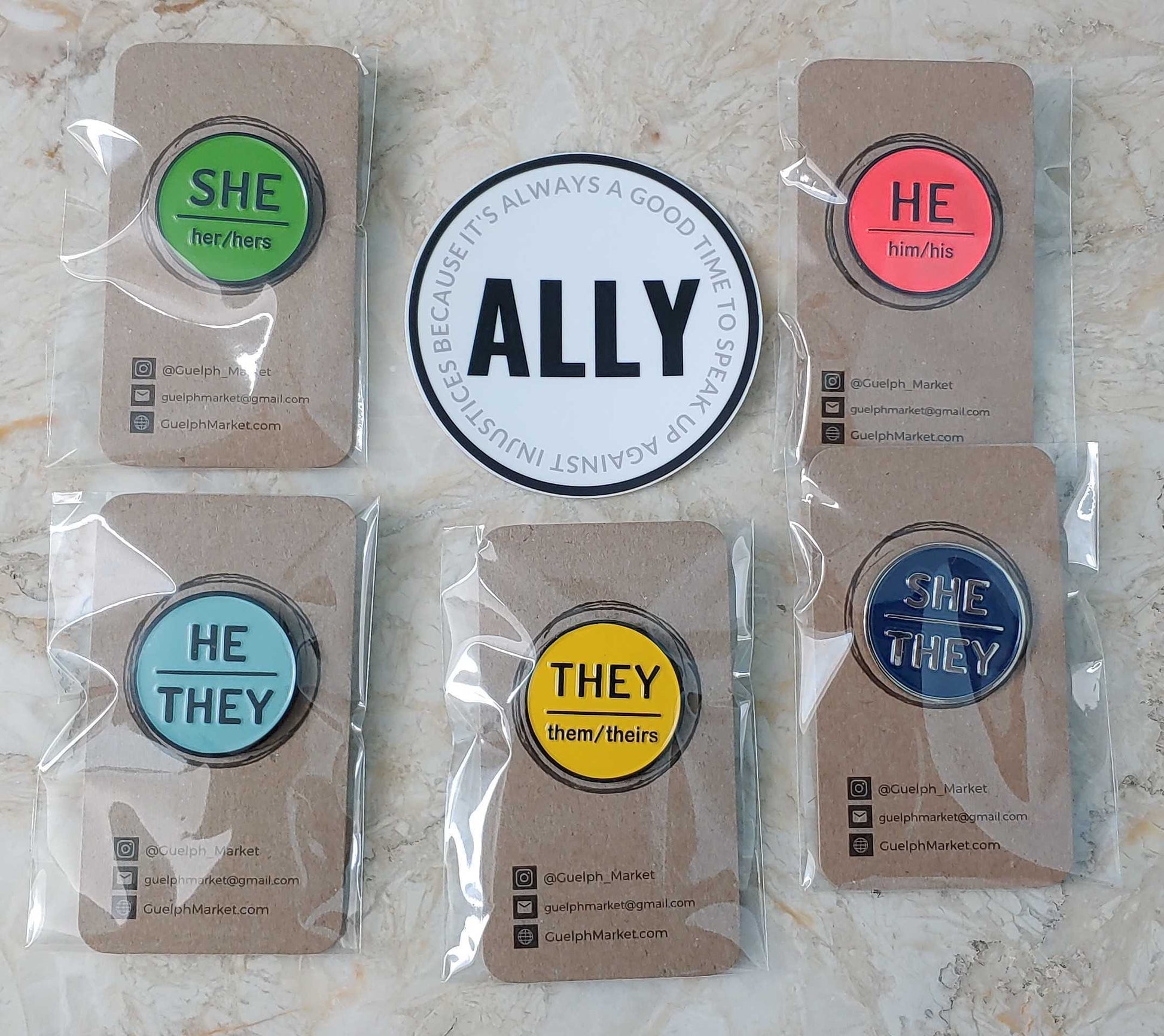 Photo of 5 pins in plastic sleeve, attached to brown cardboard. In the middle is a white circle with the word ALLY