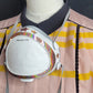 Photo of glittery sticker on a white flo mask; mask is hanging around the neck of a manikin; manikin is wearing a pink shirt with yellow stripes