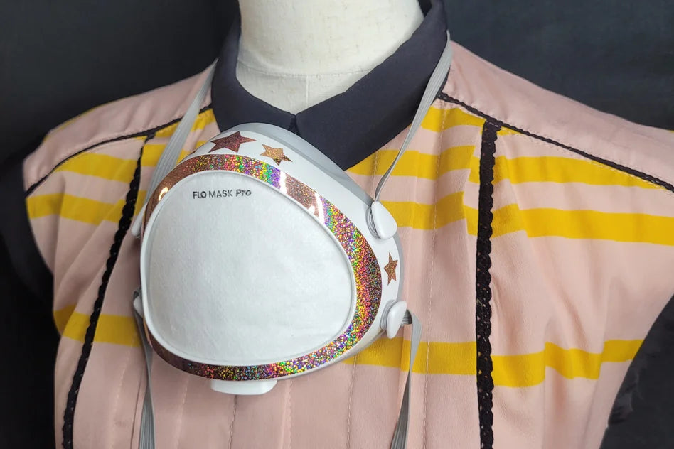 Photo of glittery sticker on a white flo mask; mask is hanging around the neck of a manikin; manikin is wearing a pink shirt with yellow stripes