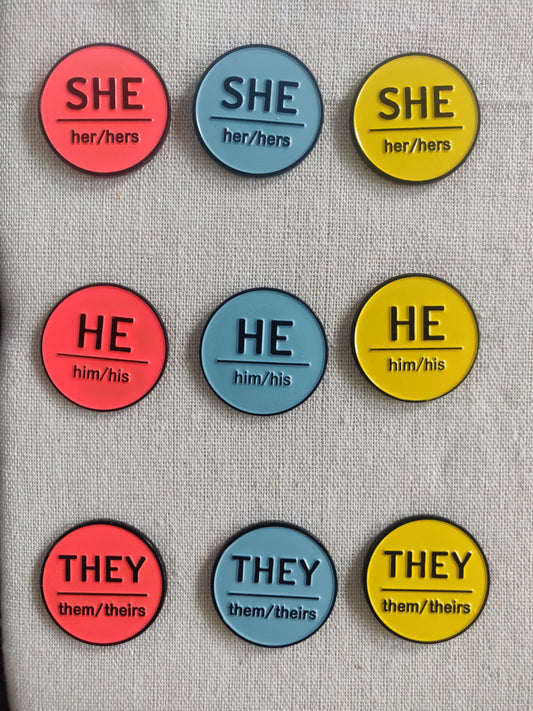 Photo of 3x3 rows of pins, with top row of She, middle row of He and bottom row of They